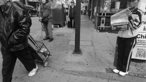 A busy street scene in black and white, featuring pedestrians, a cart, and a person holding a flyer.