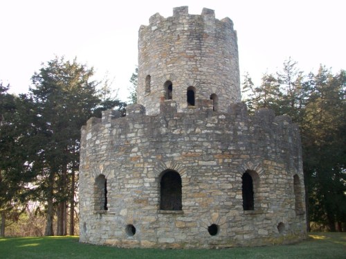 A stone tower with a round base and crenellated top, surrounded by trees and grass.