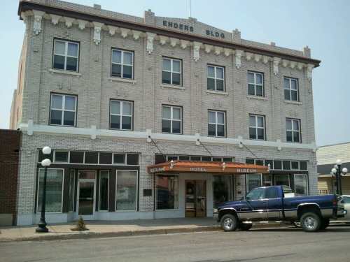 Historic brick building with large windows, an awning, and a blue pickup truck parked in front.