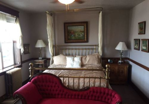 A cozy bedroom featuring a brass bed, red couch, lamps, and framed artwork on the walls.
