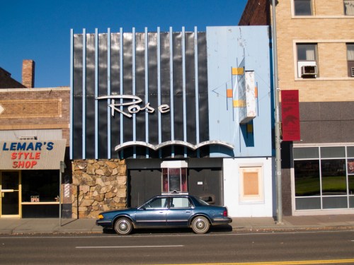 A vintage building with "Rose" signage, featuring a blue and black facade, next to a style shop and a parked blue car.