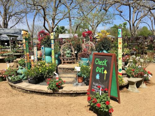 A vibrant garden center with colorful flowers, decorative poles, and a "Check Out" sign amidst lush greenery.