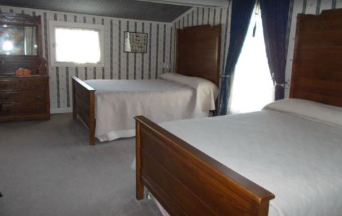A cozy bedroom with two wooden beds, a dresser, and patterned wallpaper, featuring blue curtains by the window.