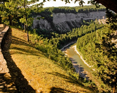 A scenic view of a river winding through a lush green valley, flanked by steep cliffs and trees.