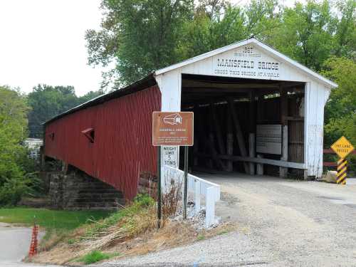 A red covered bridge with a white roof, surrounded by greenery and a sign indicating weight limits.