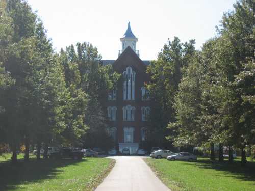 A historic brick building surrounded by trees, with a pathway leading up to it on a sunny day.