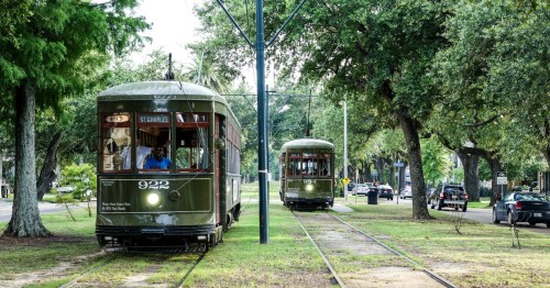 Two vintage streetcars on tracks surrounded by trees, with one approaching the other in a lively urban setting.