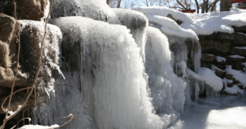 A frozen waterfall cascading over rocks, surrounded by snow and ice, creating a serene winter scene.