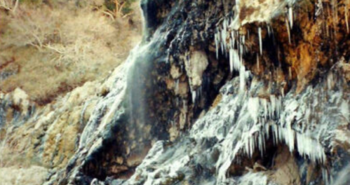A rocky cliff with icicles hanging down, surrounded by a natural landscape.