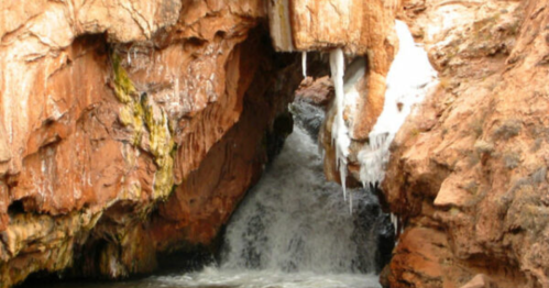 A rocky cave with icicles hanging above a small waterfall flowing into a pool of water.