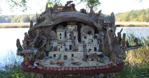 A whimsical miniature village made of natural materials, set by a serene lake surrounded by trees.