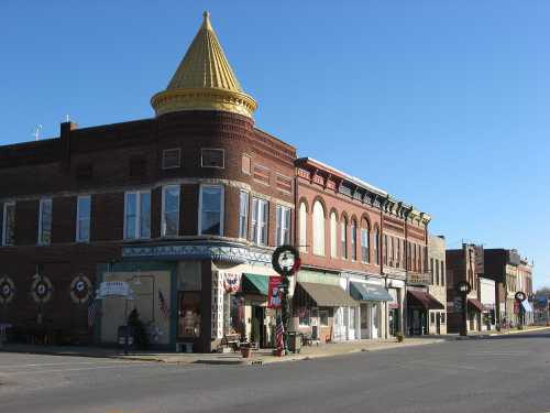 Historic downtown street with brick buildings, a yellow turret, and festive decorations. Clear blue sky above.