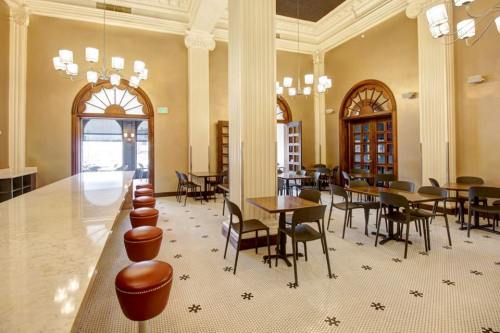 A spacious café with tall columns, elegant lighting, and wooden tables surrounded by black chairs.