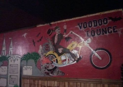 A colorful mural of a skeleton on a motorcycle, with bats and a "Voodoo Lounge" sign in a dimly lit setting.