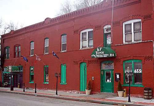 A red brick building with green accents, featuring a sign for "B.J.'s Bayou" and several flags hanging outside.