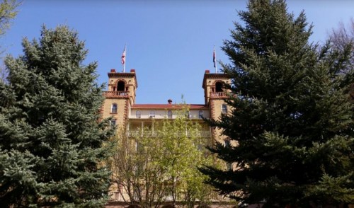 Historic building with towers, surrounded by tall evergreen trees and clear blue sky.