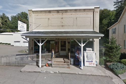 A small, rustic storefront with a porch, featuring a sign and an ice vending machine outside.
