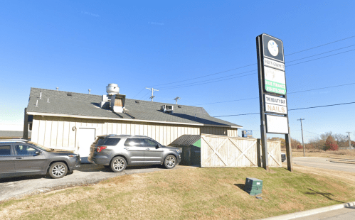 A building with a sign for a beauty bar and nails, featuring parked cars and a clear blue sky.