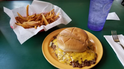 A plate with a cheeseburger and a side of golden fries, accompanied by a blue cup of water on a green table.
