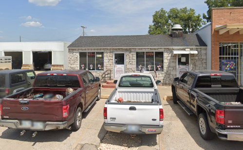 A small stone building with "OPEN" signs, surrounded by parked pickup trucks in a parking lot.