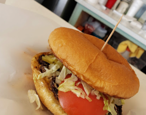 A close-up of a burger with lettuce and tomato, held together by a toothpick, on a white paper surface.