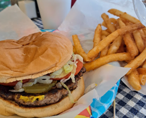 A close-up of a hamburger with lettuce, tomato, pickles, and mustard, served with a side of crispy French fries.