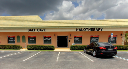 Exterior of a building with signs for "Salt Cave" and "Halotherapy," featuring a black car parked in front.