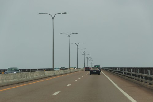 A view of a bridge road with cars and streetlights, fading into a foggy horizon.