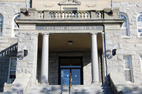Stone steps lead to the entrance of Newport City Hall, featuring columns and decorative signage above the door.