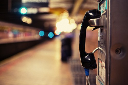 A close-up of a black payphone with a blurred train station background and soft, glowing lights.