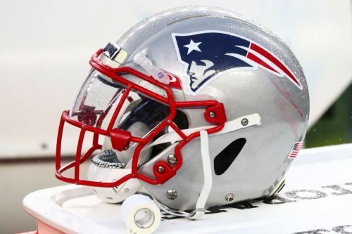 A silver football helmet with a red face mask and the New England Patriots logo on the side, resting on a surface.