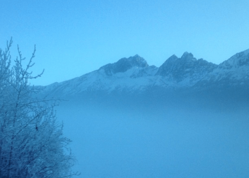 A serene winter landscape featuring snow-covered mountains shrouded in mist under a blue sky.