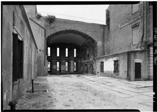 Black and white image of an abandoned building interior with arched ceilings and crumbling walls.