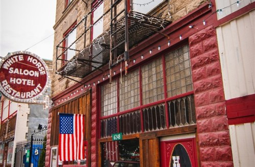 Exterior of the White Horse Saloon Hotel, featuring a vintage sign, American flag, and festive lights.