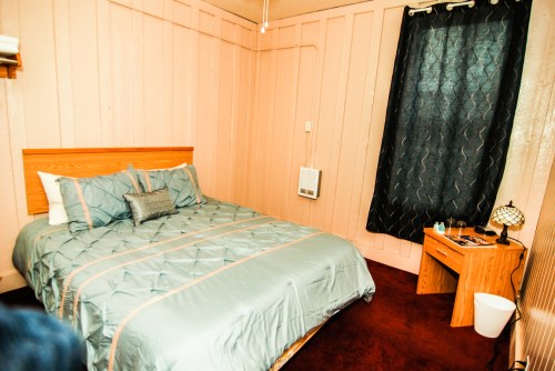 Cozy bedroom with a double bed, pink walls, dark curtains, and a small bedside table.