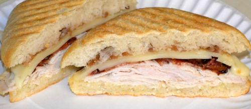 A sliced sandwich with grilled chicken, melted cheese, and caramelized onions on a toasted bread.