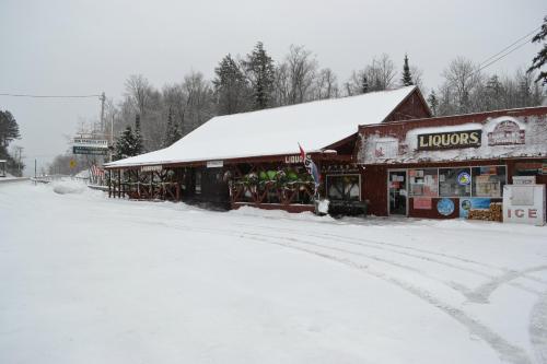 A snowy scene of a liquor store with a red exterior, surrounded by trees and a quiet road.
