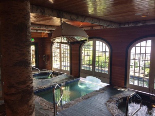 A serene spa interior featuring hot tubs, wooden accents, and large windows overlooking a garden.