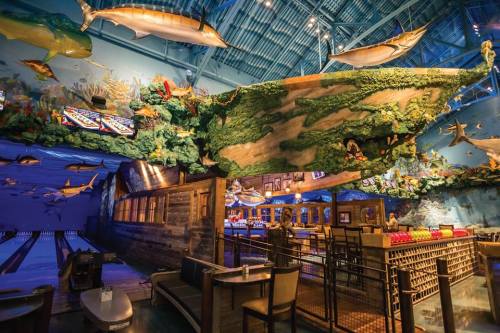 A vibrant indoor space featuring a bowling alley, bar, and a ceiling adorned with fish and greenery.