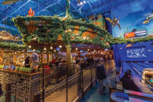 A vibrant indoor restaurant with a ship-themed design, surrounded by greenery and marine decor, bustling with patrons.