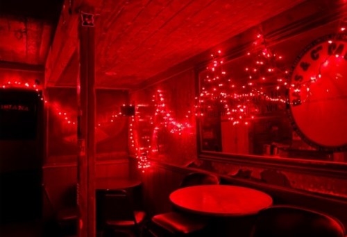 Dimly lit room with red lights and a mirror, featuring empty chairs and a rustic wooden interior.