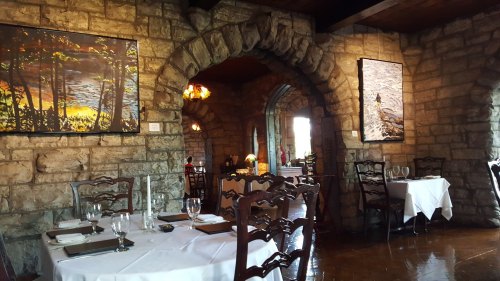 Cozy restaurant interior with stone walls, wooden furniture, and artwork, featuring tables set for dining.