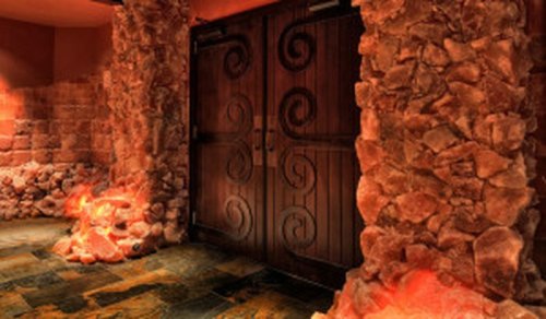 Wooden double doors with decorative swirls, surrounded by textured stone walls and soft glowing lights.