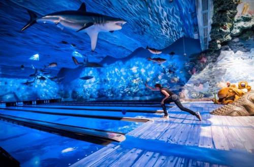 A person bowls in a vibrant underwater-themed bowling alley with sharks and colorful sea life decor.
