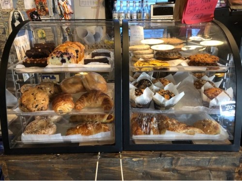 A display case filled with various baked goods, including cookies, pastries, and muffins, in a cozy café setting.