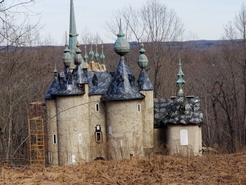 A whimsical, unfinished castle with spires, set in a wooded area during winter.