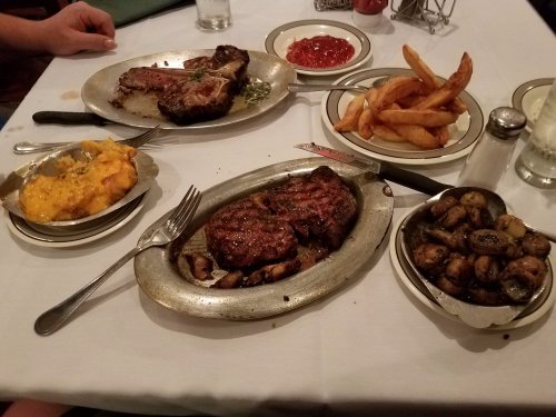 A table set with two plates of steak, sides of mashed potatoes, fries, and a small bowl of ketchup.