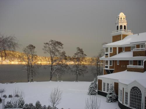 A snowy landscape featuring a lakeside building with a tower, surrounded by trees and a calm, reflective lake.