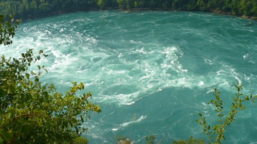 Aerial view of swirling turquoise water surrounded by lush green foliage.