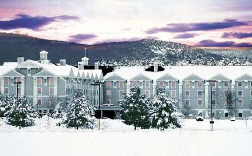 A snow-covered hotel surrounded by trees, with mountains in the background and a colorful sunset sky.